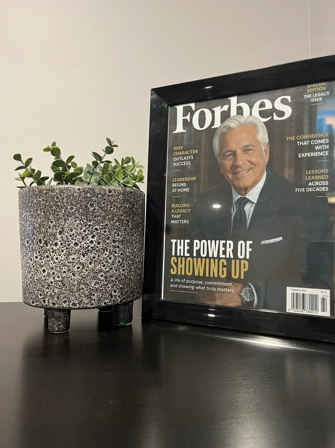 Framed Forbes-style executive portrait displayed beside a planter